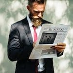 Image of a man in a suit with a red tie reading a business newspaper